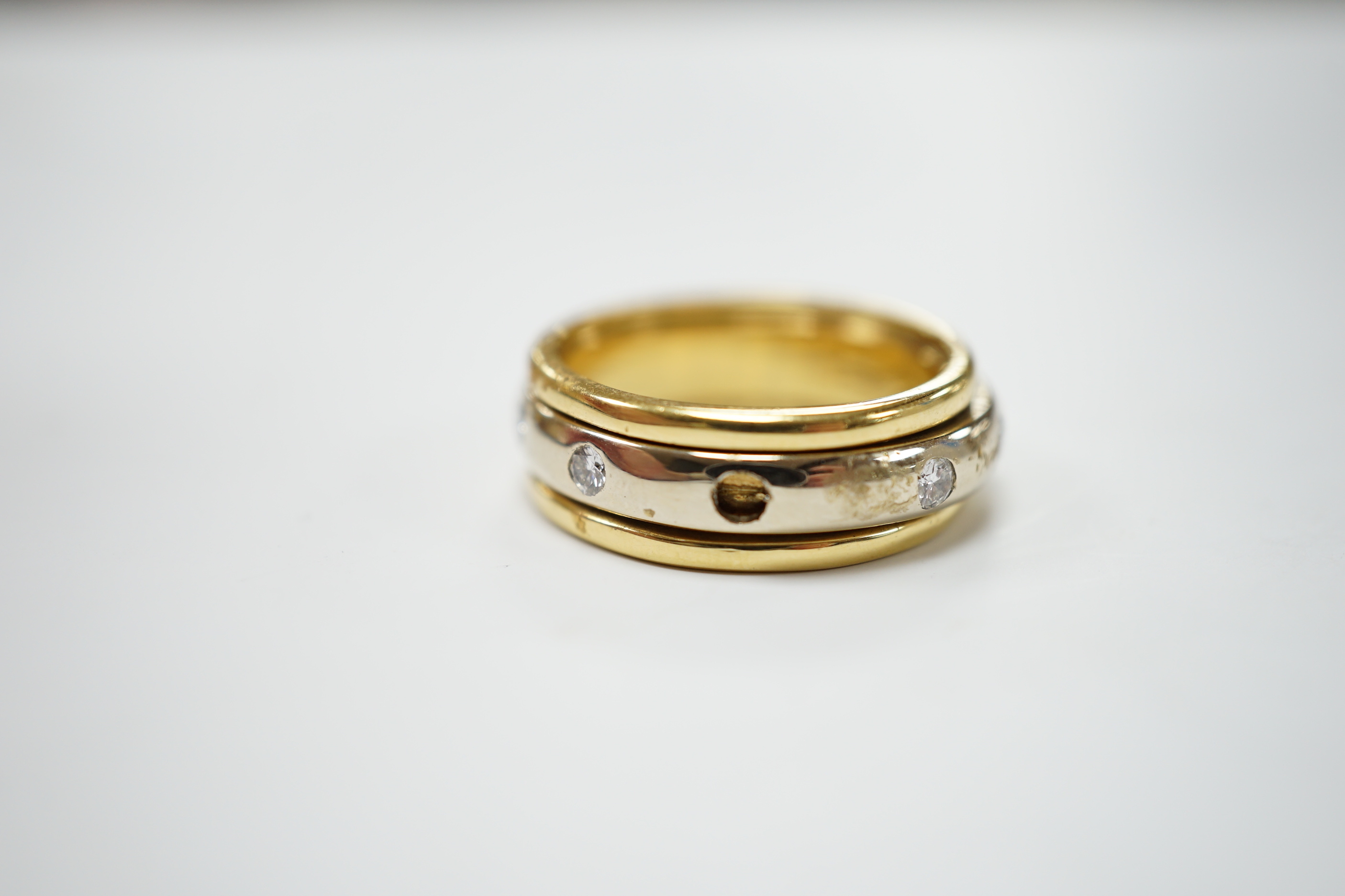 A modern 750 yellow metal ring, with central diamond set rotating white metal band (stone missing), size P/Q, gross weight 7.9 grams.